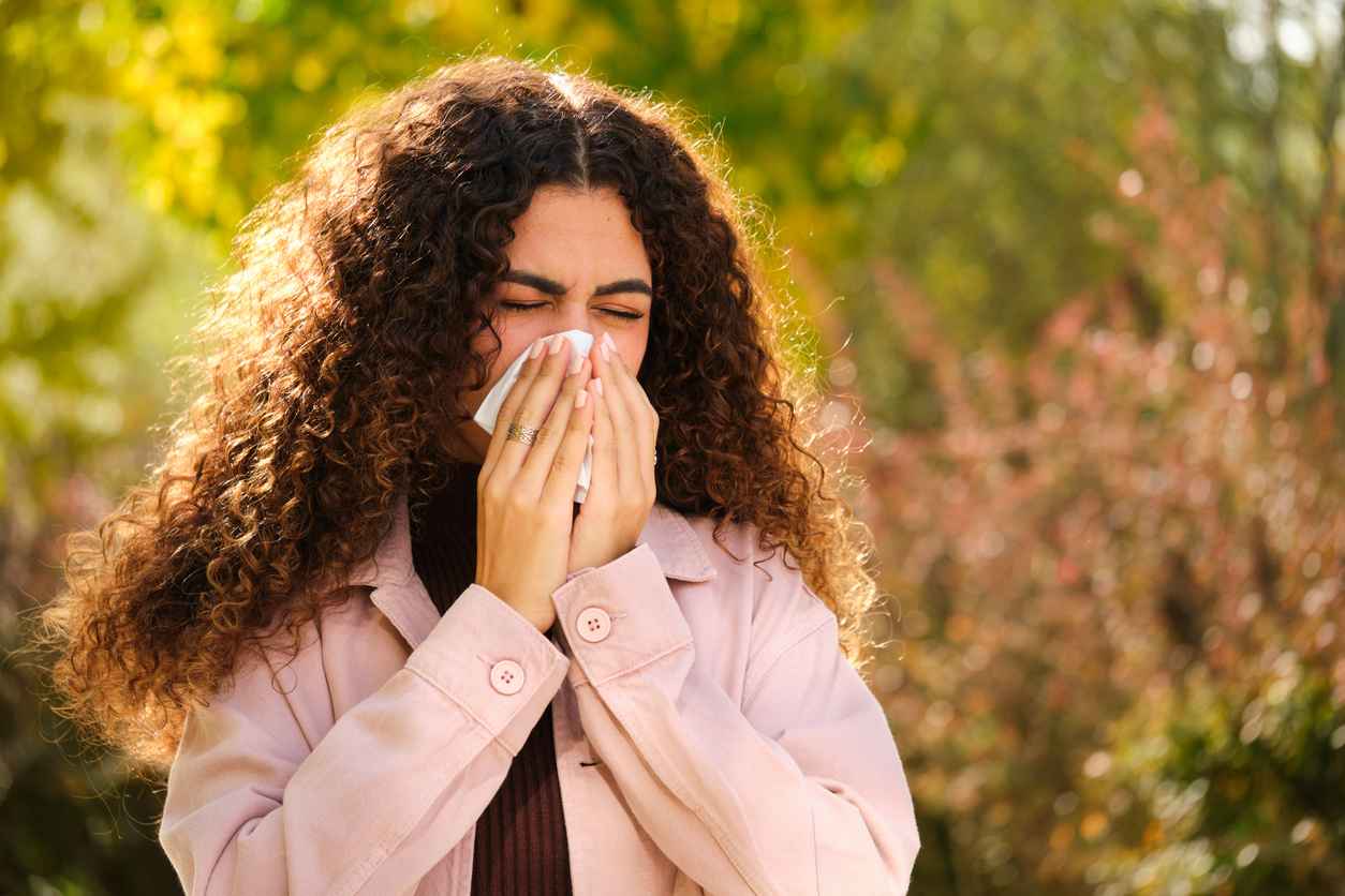 woman sneezing outside due to fall allergies, covering her mouth with a tissue