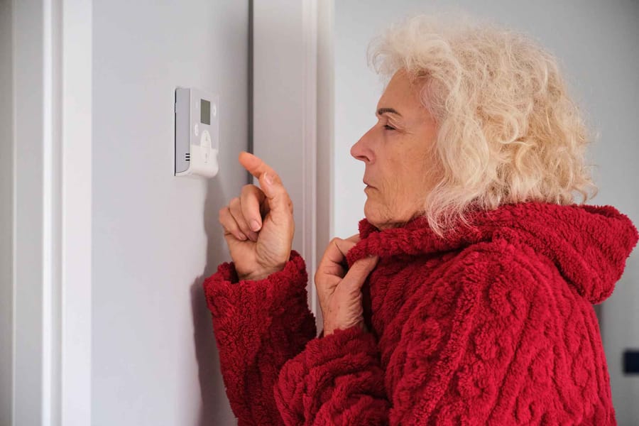 woman feeling cold in winter at home adjusting the thermostat