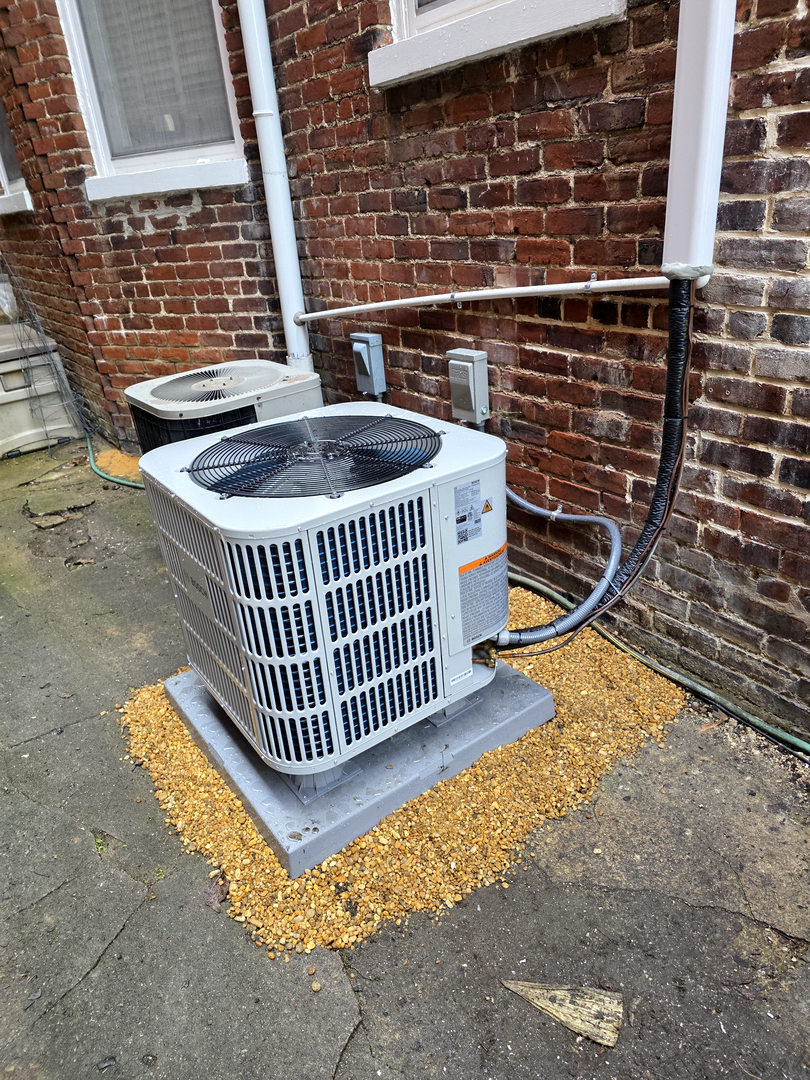 outdoor air conditioning unit installed on gravel and concrete near a brick wall