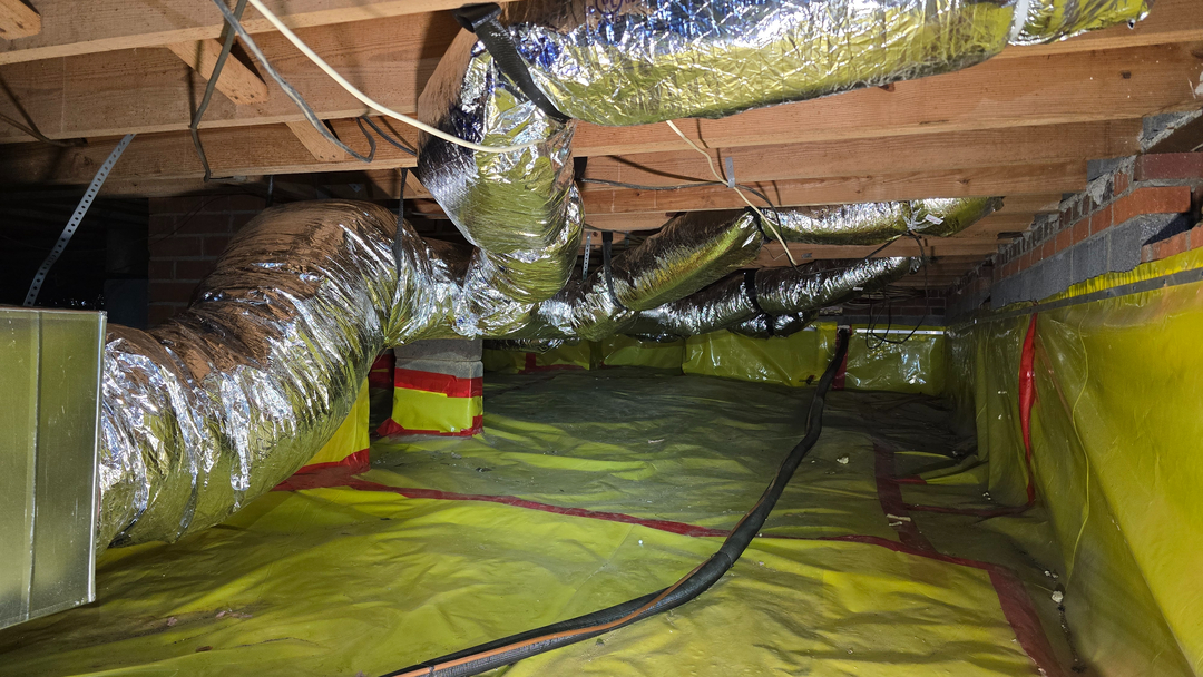 Crawl space with insulated HVAC ductwork and secured moisture barrier for a heating system in a residential area, showcasing professional installation services in Midlothian.